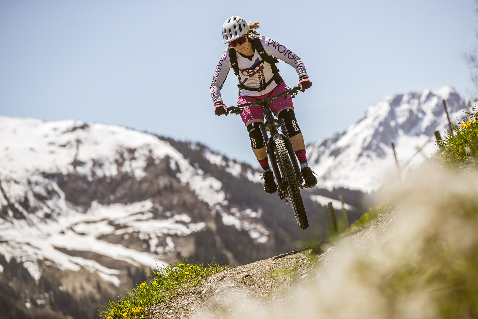 Mountainbikerin springt vor schneebedeckten Gipfeln