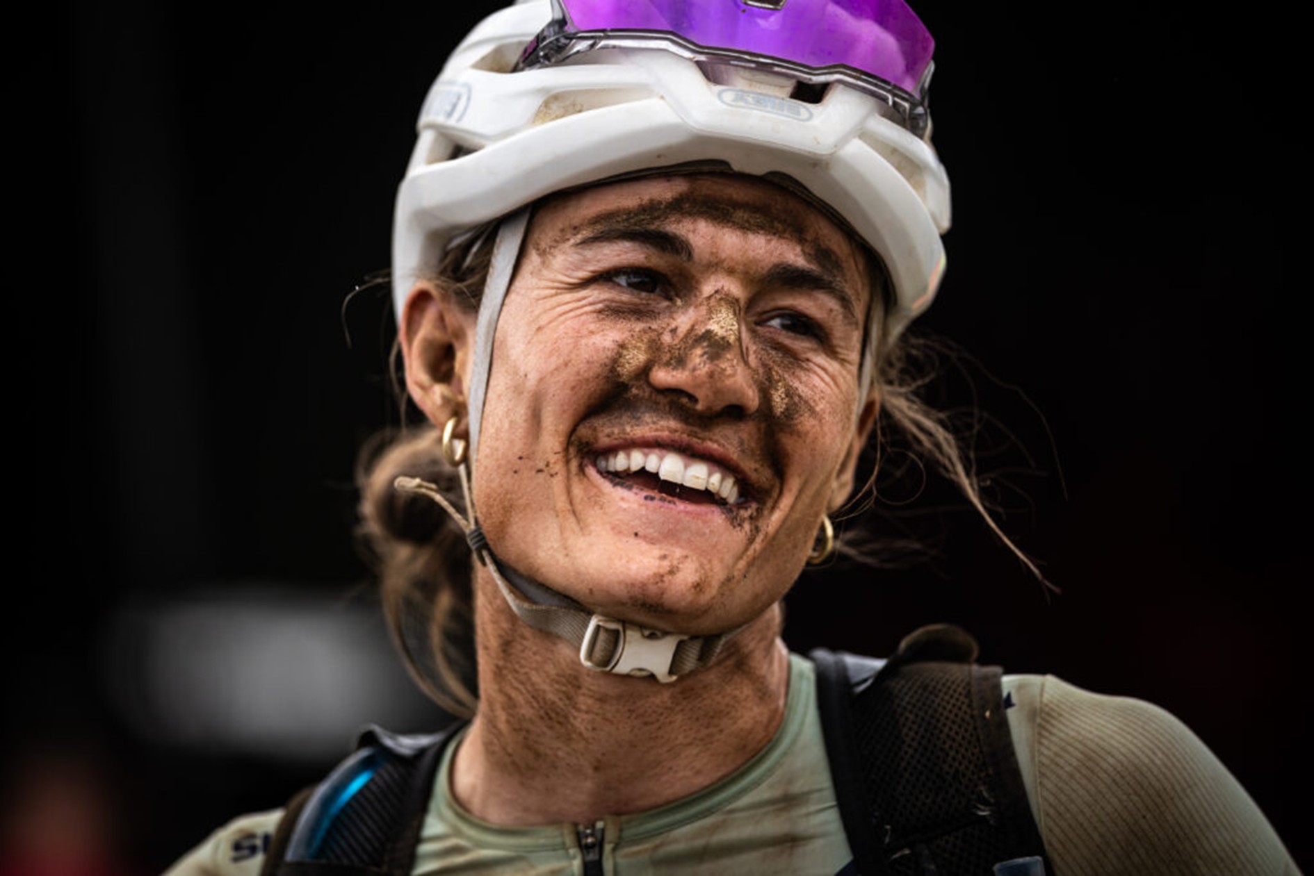 Lachende Fahrerin mit Schlamm im Gesicht nach einer Etappe des Cape Epic