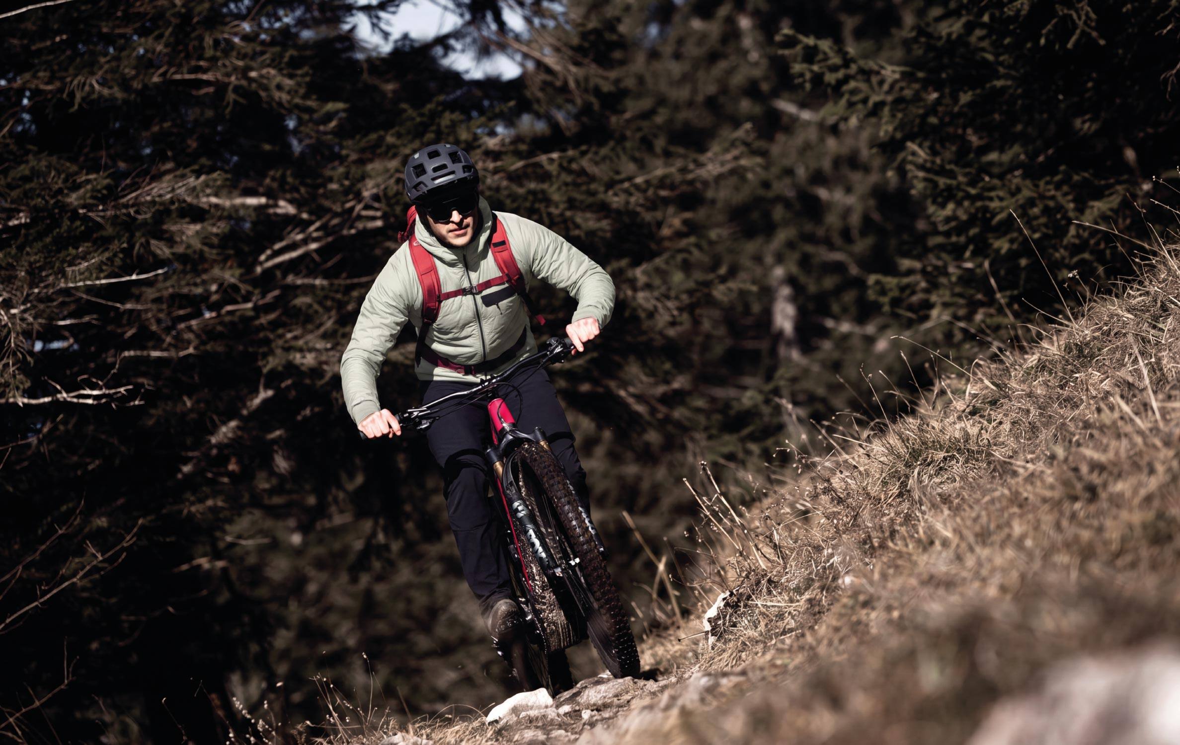Mountainbiker in salbeigrüner Jacke auf einem Waldtrail