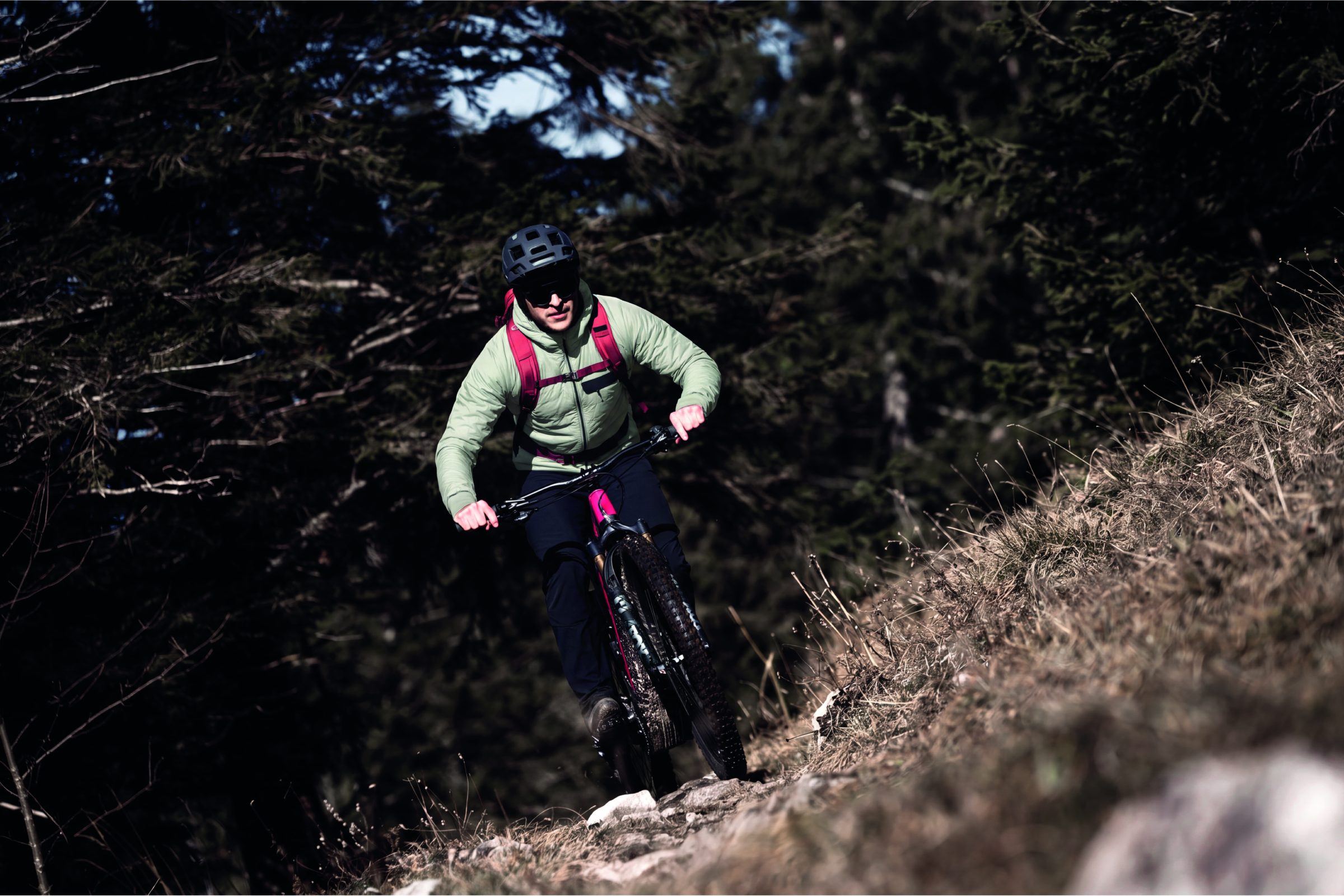 Mountainbiker in heller Jacke auf einem Waldtrail