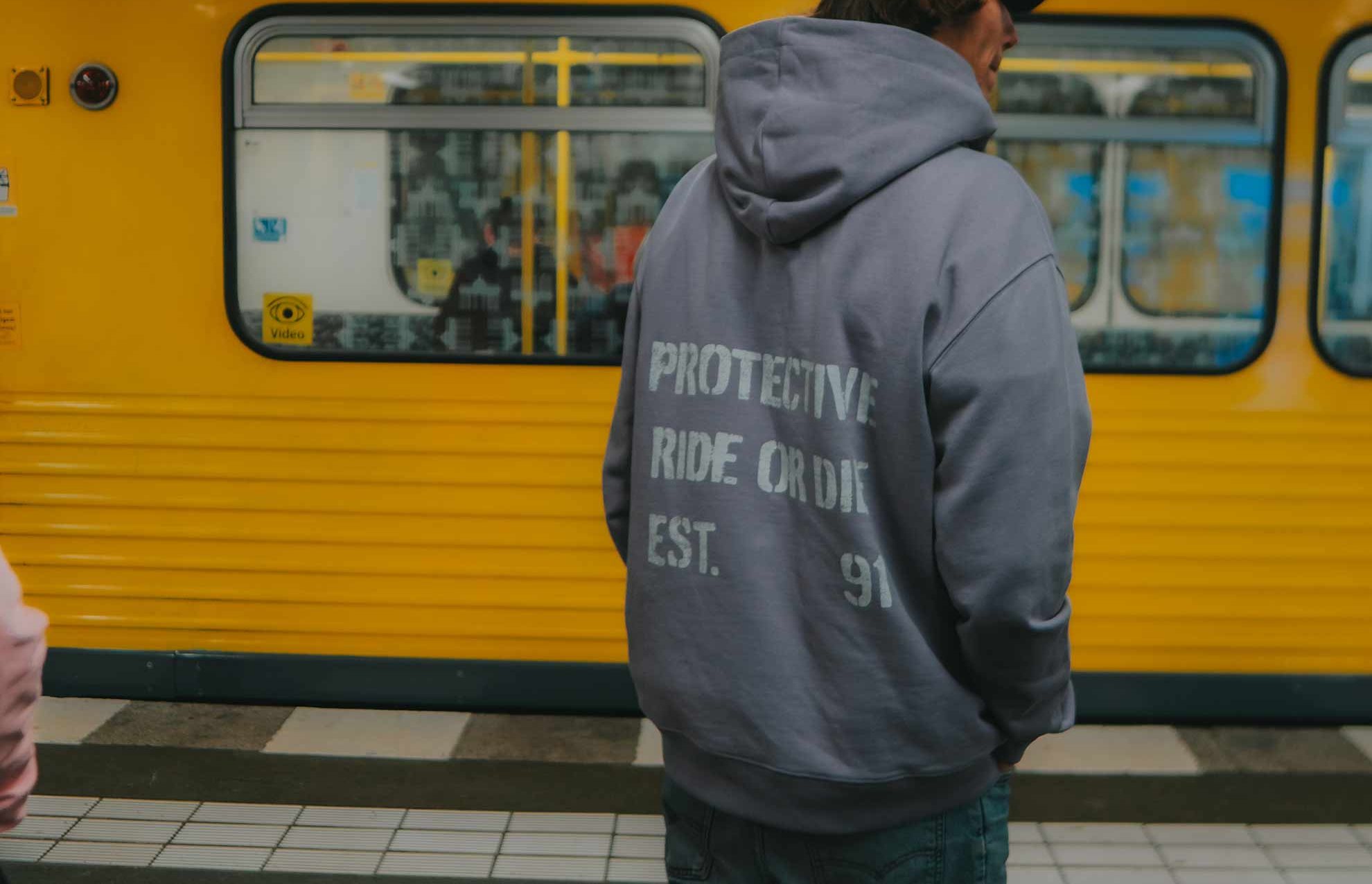 Hoodie mit PROTECTIVE-Aufdruck am Bahnsteig